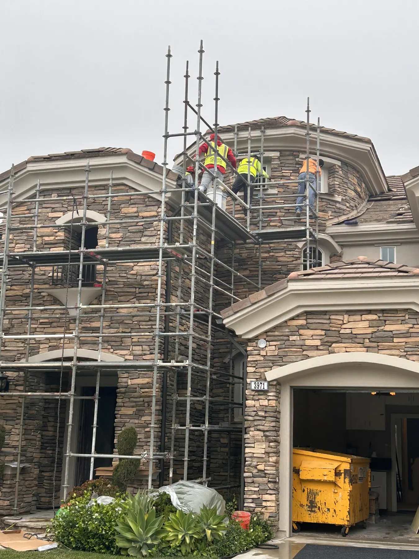 Masonry crew on scaffolding installing stone veneer on a large two-story home