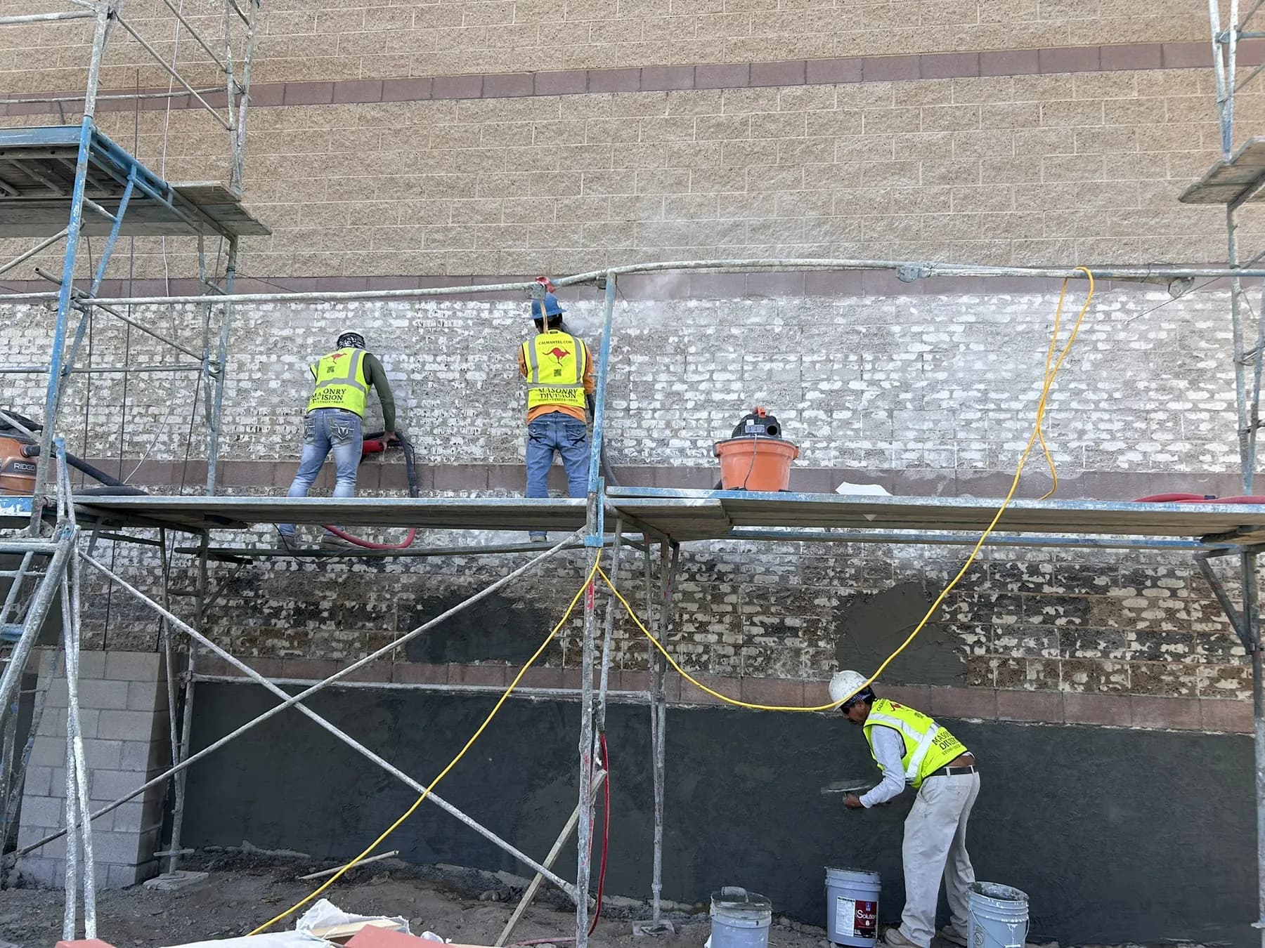 Masonry crew plastering and finishing a commercial block wall from scaffolding