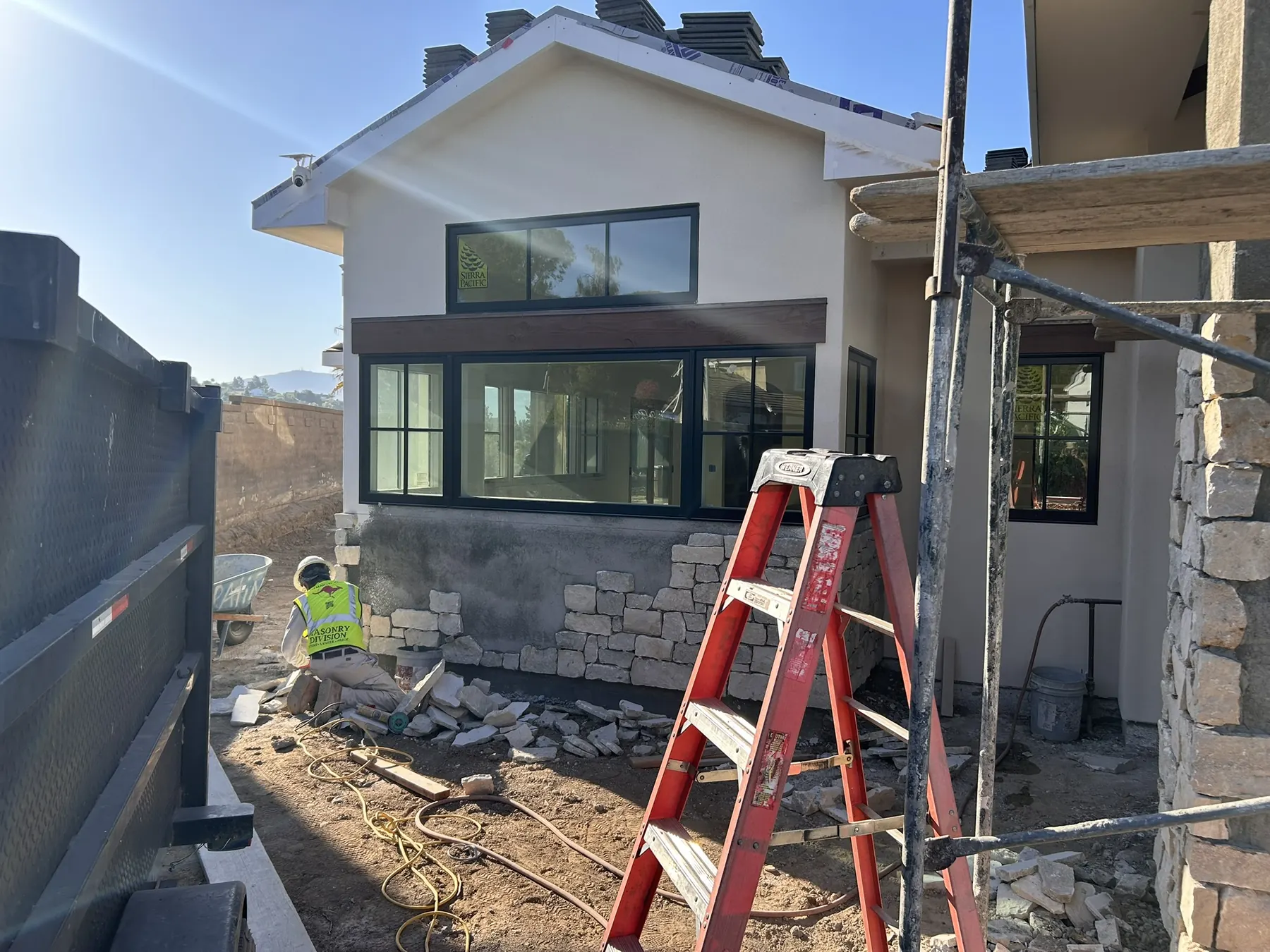 Mason installing stone veneer wainscot on a home exterior