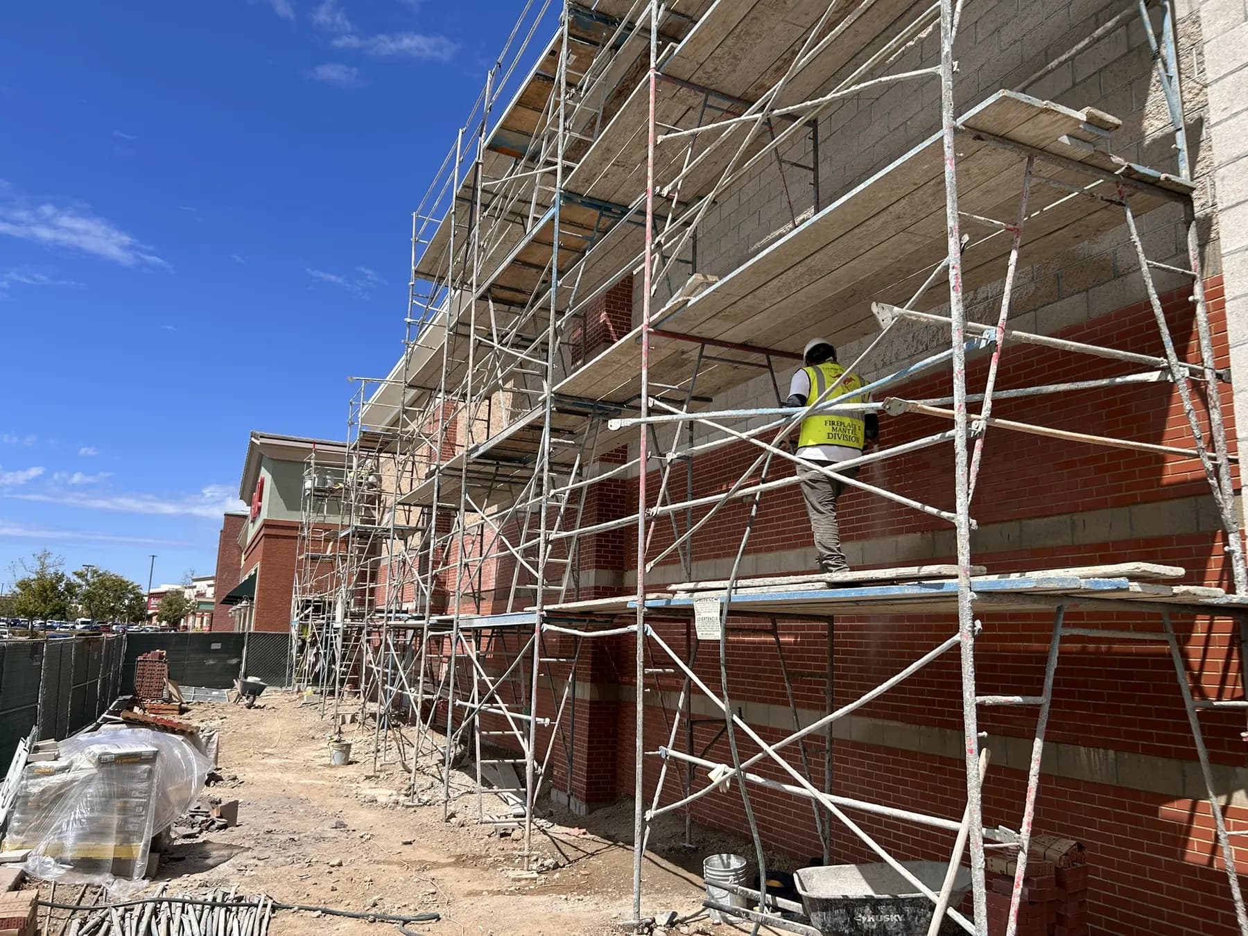 Mason on scaffolding finishing a brick veneer wall on a retail building
